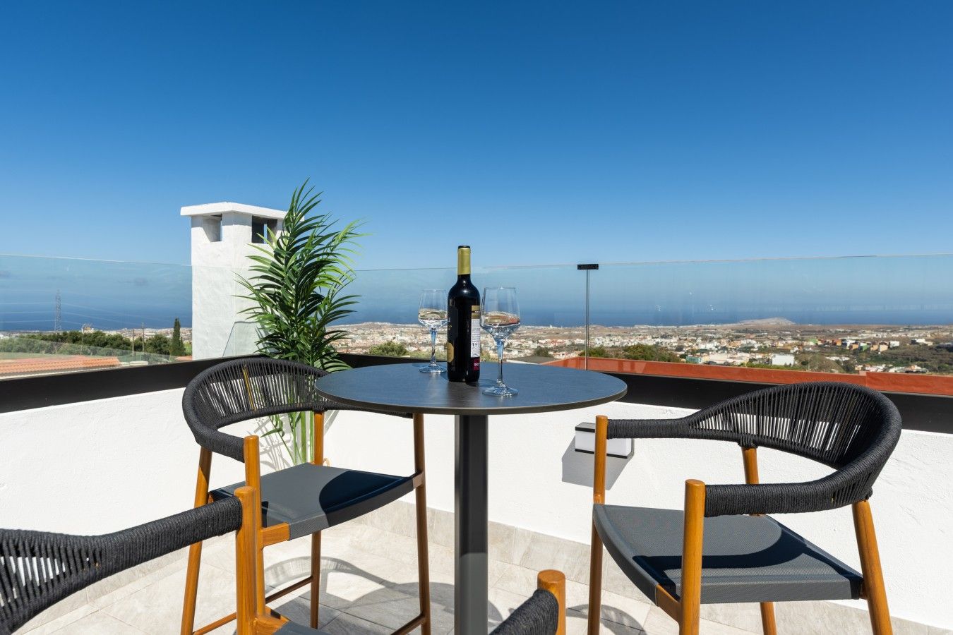 A terrace with a table and chairs, a bottle of wine, and a view of the coastline.