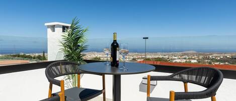A terrace with a table and chairs, a bottle of wine, and a view of the coastline.