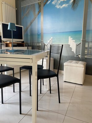 A room with a glass table, chairs, a television, and a beach mural on the wall. - Fairmont Residence Elisabetta by Ca-sa Check (Chioggia)