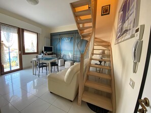 A spacious living area with a wooden staircase, a dining table with chairs, a sofa, and a TV. - Fairmont Residence Elisabetta by Ca-sa Check (Chioggia)