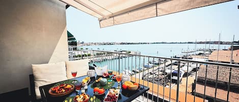 Un balcón con una mesa preparada para una comida, con vista a un puerto deportivo con barcos y un paisaje urbano al fondo.