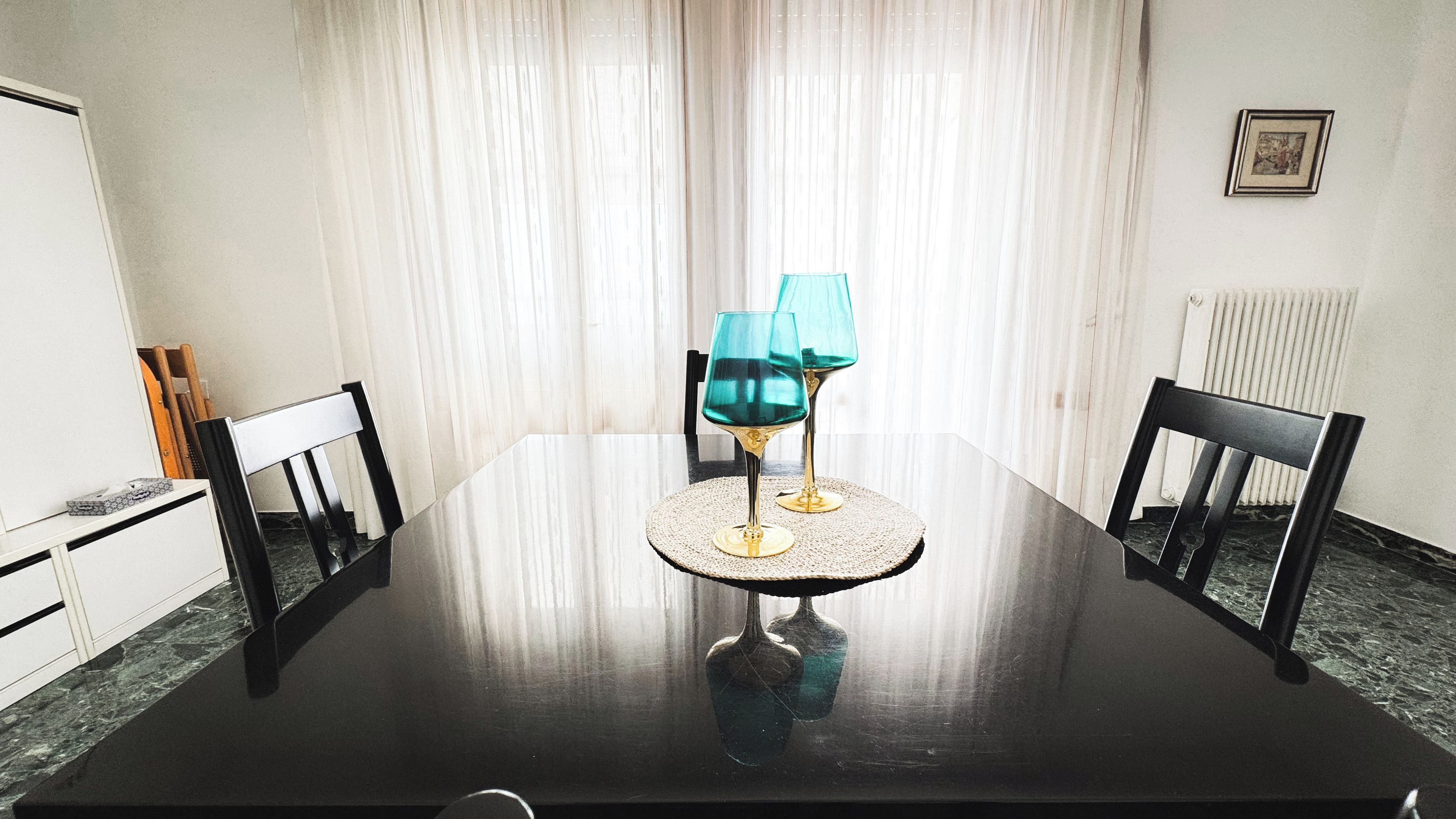 Una mesa de comedor con dos sillas, un jarrón y dos vasos sobre un mantel tejido.