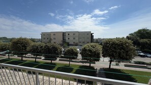 Um edifício com teto plano e várias janelas, cercado por árvores e um espaço pavimentado com bancos.