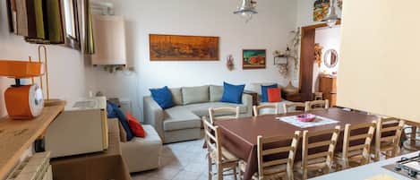 A living room with a sofa, a dining table with chairs, and a kitchen area with a stove.
