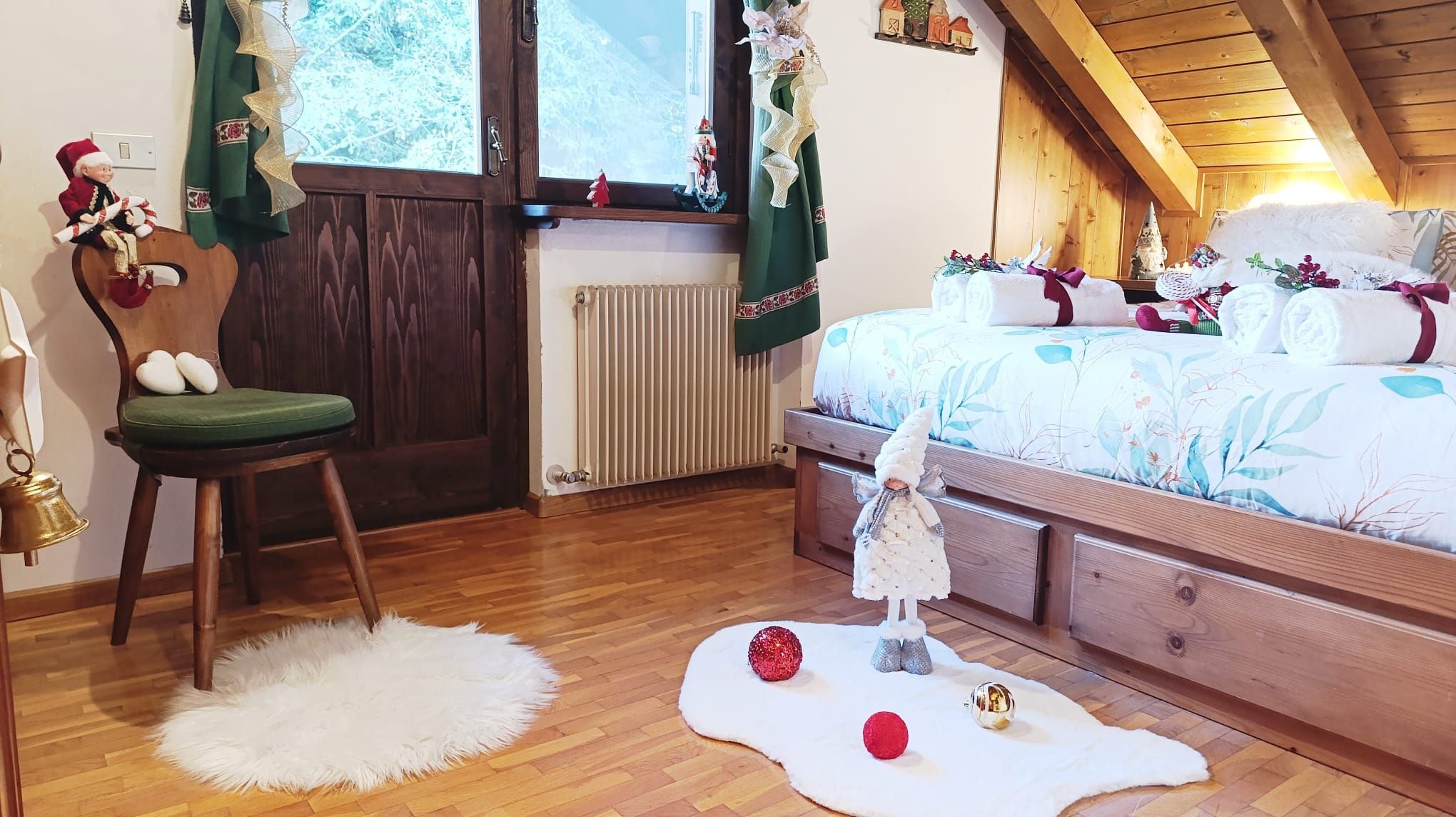 A cozy bedroom with a wooden bed, a green chair, and a small white table with a bell.