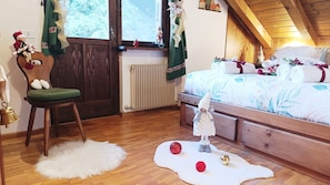 A cozy bedroom with a wooden bed, a green chair, and a small white table with a bell. - Chalet Stravedo by Ca-sa Check (San Vito di Cadore)