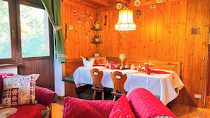 Um quarto acolhedor de madeira com uma mesa de jantar posta para dois, um banco e uma janela com cortinas.