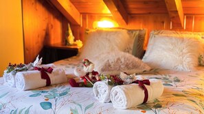 A cozy room with a wooden ceiling, a bed with floral bedding, and rolled towels with decorative bows. - Chalet Stravedo by Ca-sa Check (San Vito di Cadore)