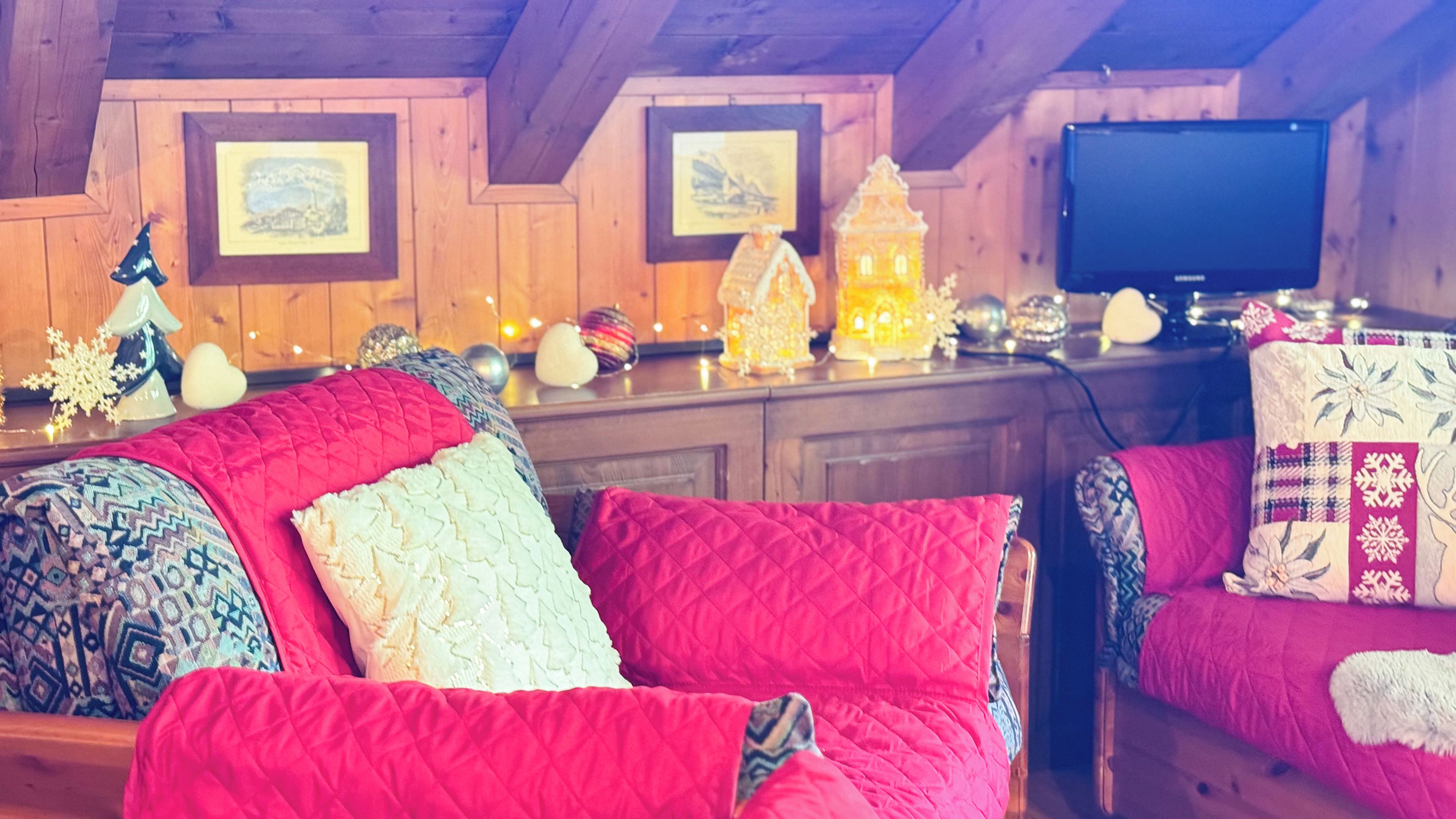 A cozy room with a wooden ceiling, a television, and a wooden cabinet with framed pictures.