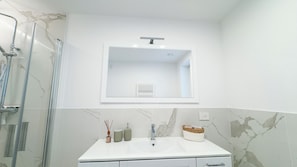 Un baño con tocador blanco, espejo, ducha y pared de mármol.
