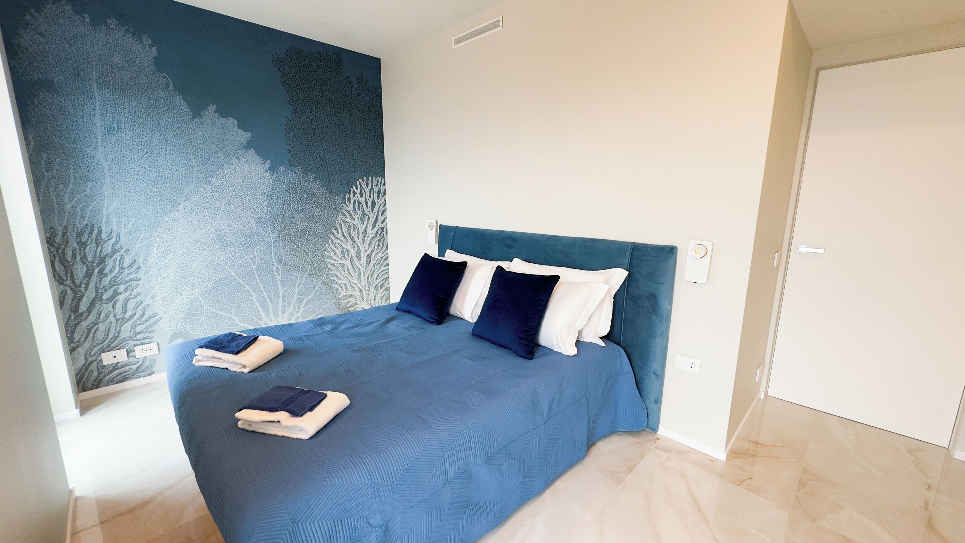 Un dormitorio con cama, almohadas, una colcha y un mural en la pared.