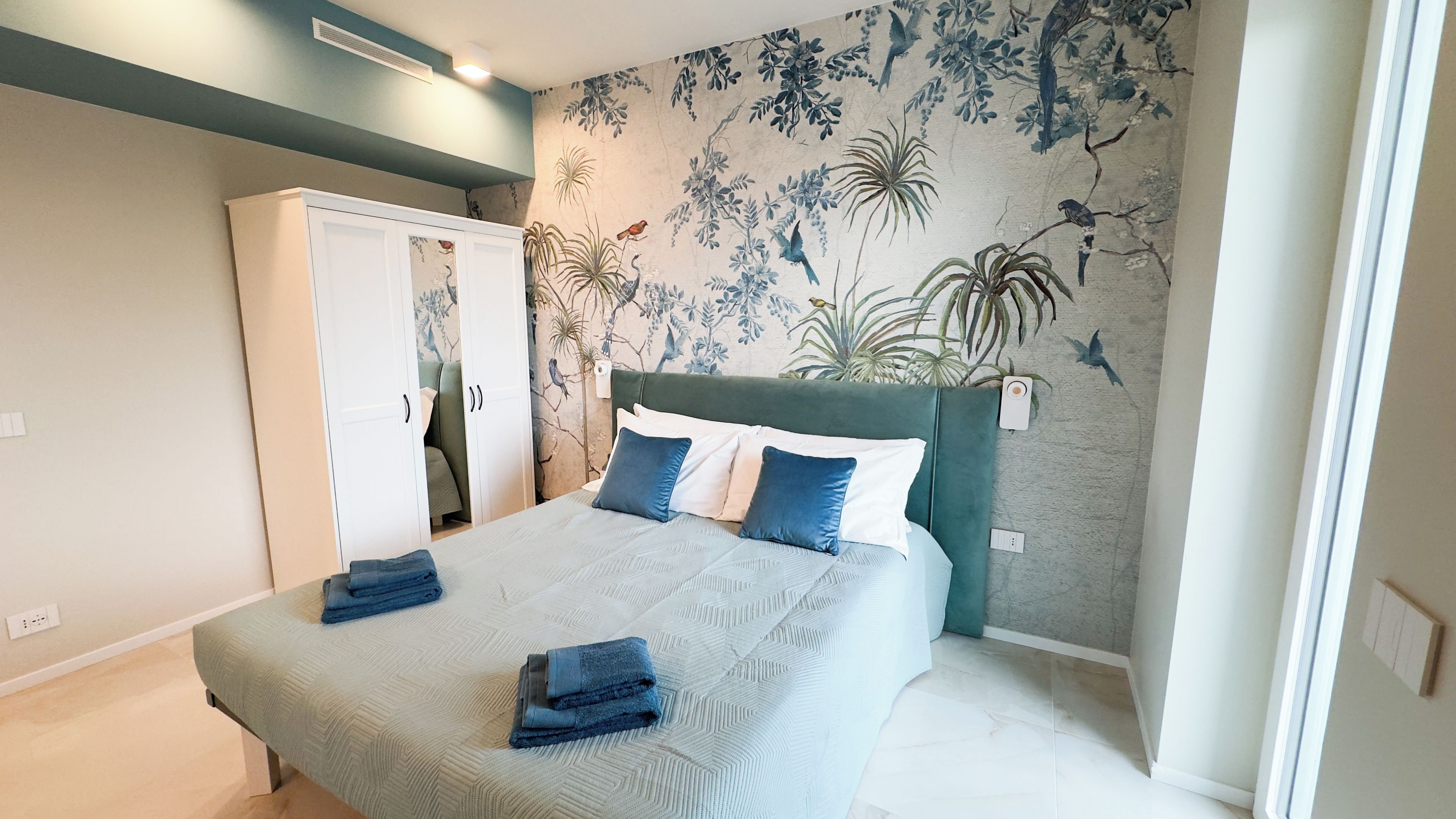 A bedroom with a bed, a wardrobe, and a wall with a nature-themed mural.