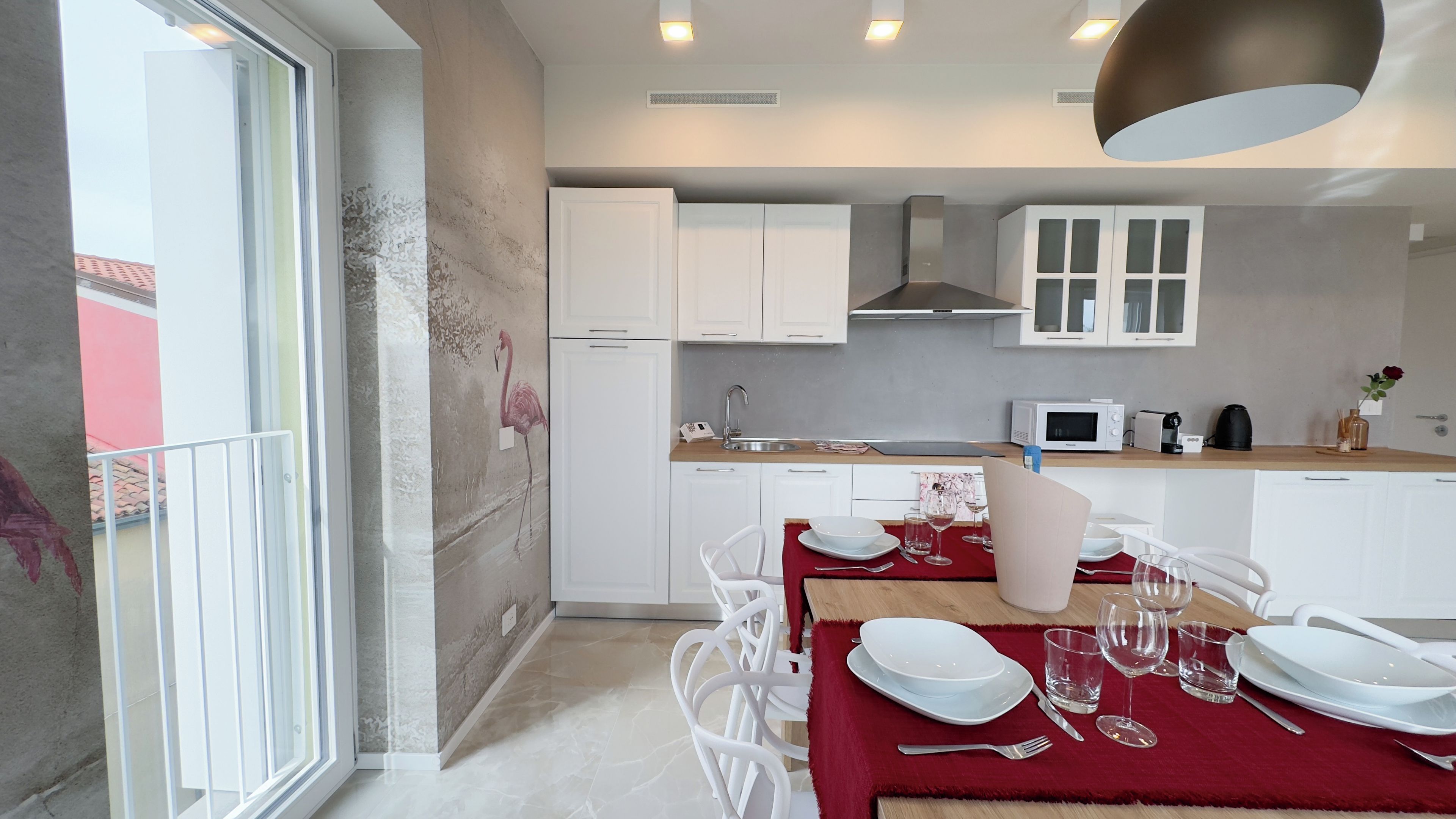 Uma cozinha moderna com armários brancos, micro-ondas e uma área de refeições com cadeiras brancas e toalha de mesa vermelha.
