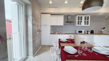 Uma cozinha moderna com armários brancos, micro-ondas e uma área de refeições com cadeiras brancas e toalha de mesa vermelha.