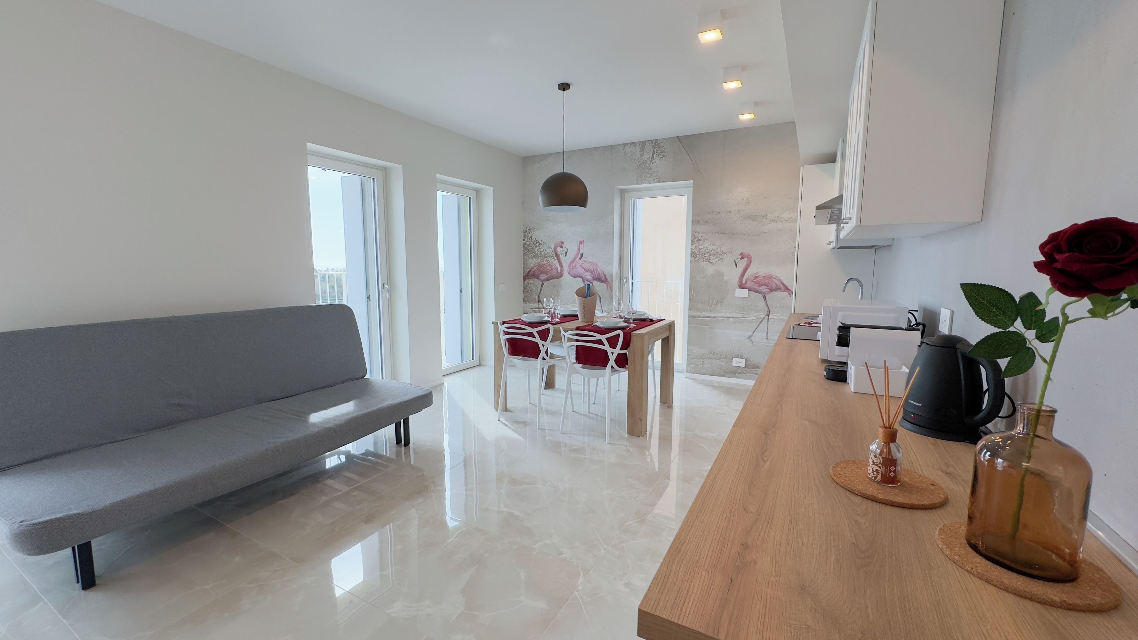 A modern kitchen with a wooden countertop, a dining area with a table and chairs, and a grey sofa.