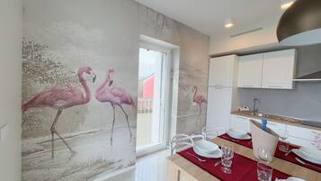 Cozinha moderna com armários brancos, área de jantar com toalha vermelha e um mural na parede com flamingos.