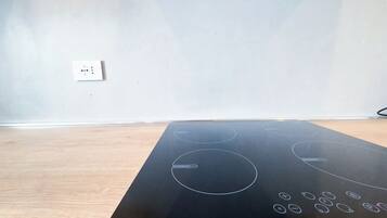 Une pièce avec une plaque de cuisson à induction noire posée sur un plancher en bois, un mur blanc et une prise de courant.