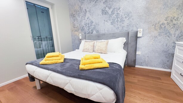 A neatly made bed with a grey headboard, white bedding, and two yellow towels on the footboard. - Farmont Seafront Venice Suite by Ca-sa Check (Chioggia)