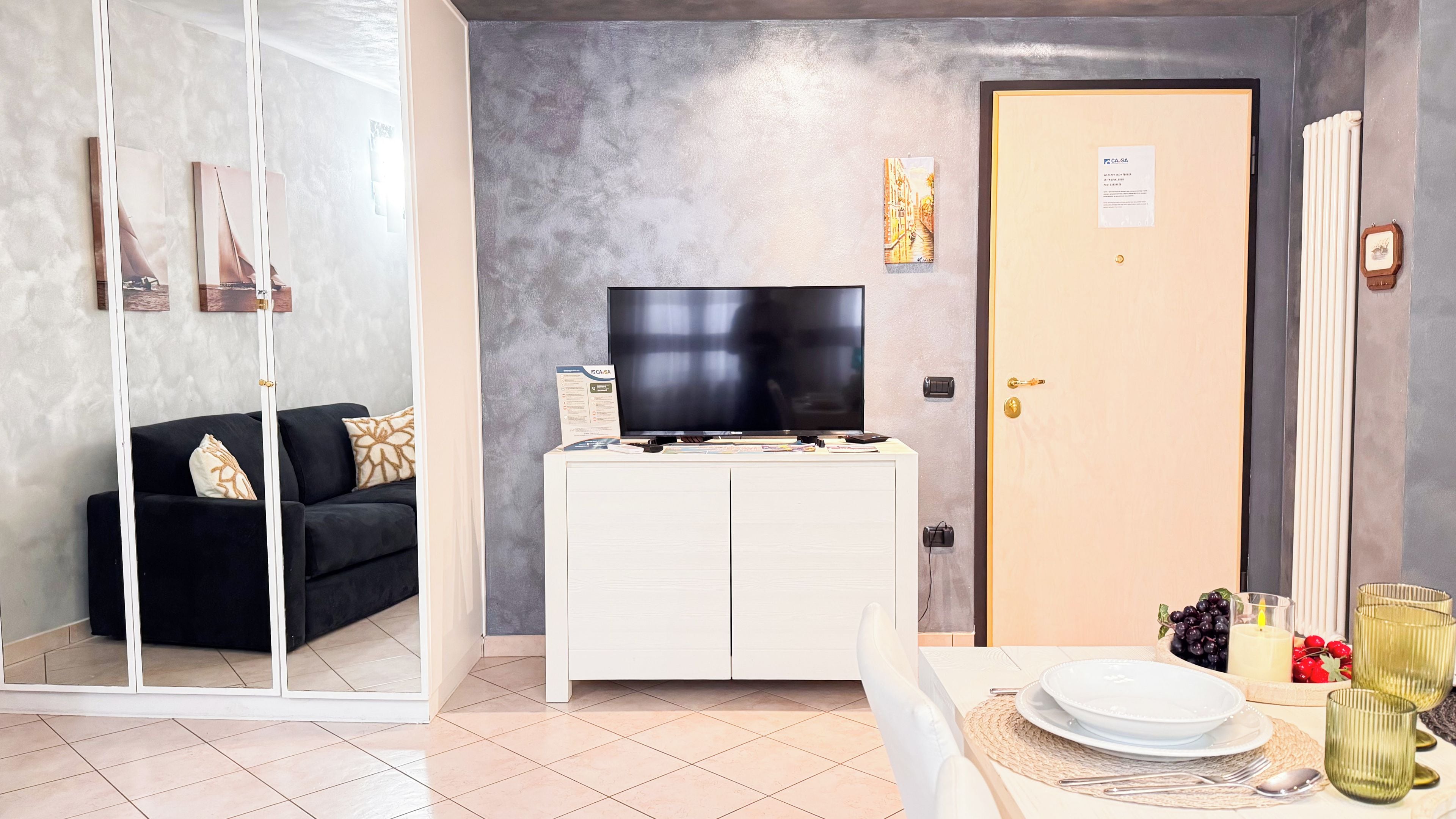 A modern living room with a flat-screen TV, a white cabinet, a black sofa, and a door with a keycard lock.