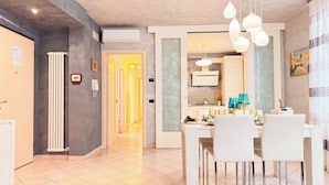 A modern dining area with a white table set for four, a kitchen in the background, and a hallway leading to another room. - Lady Teresa 2.0 by Ca-sa Check (Chioggia)