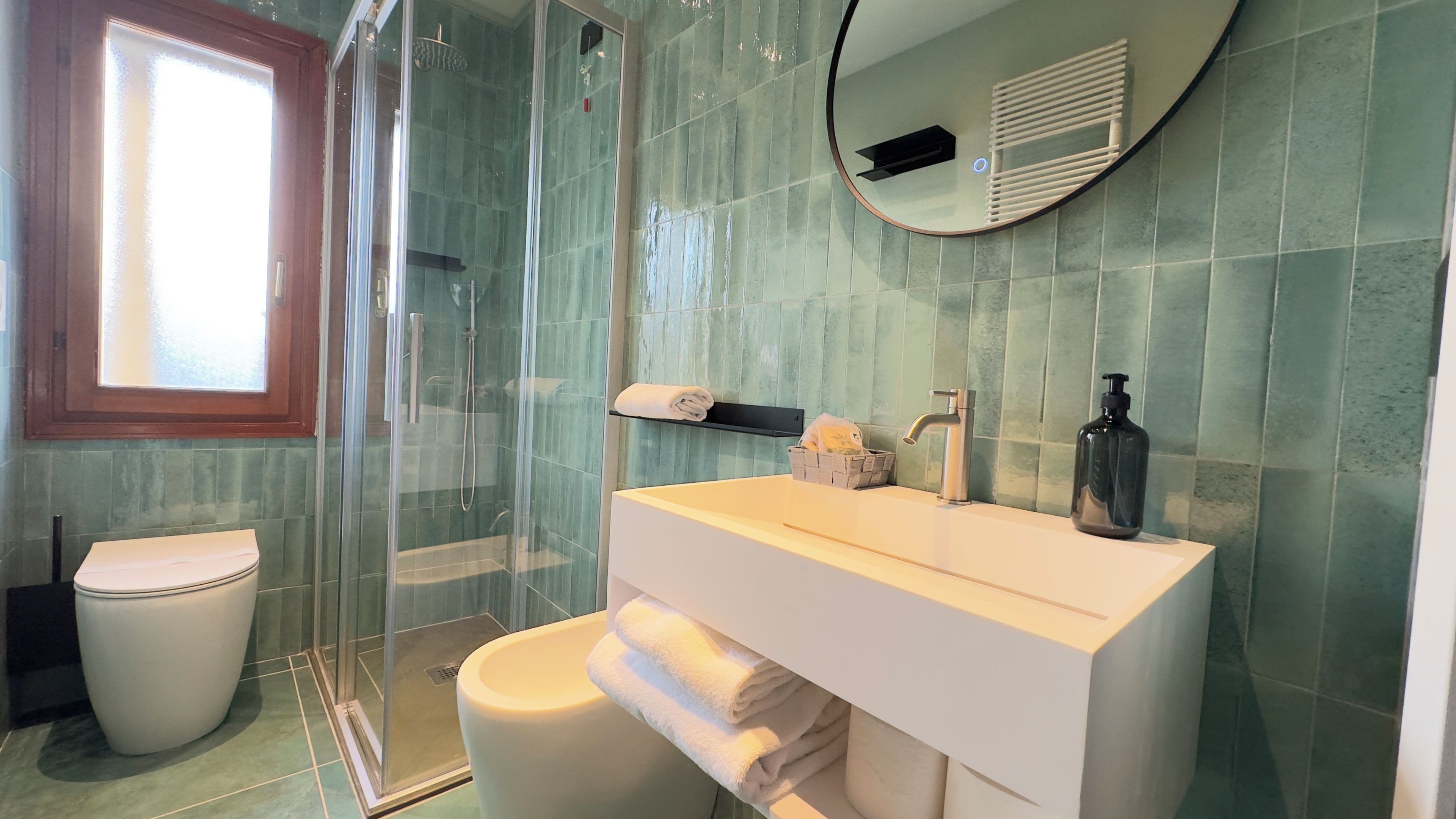 A bathroom with a glass shower enclosure, a toilet, a sink with a mirror, and a towel rack.