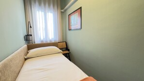 Quarto pequeno com uma cama de solteiro, mesa de cabeceira, abajur e um quadro na parede.