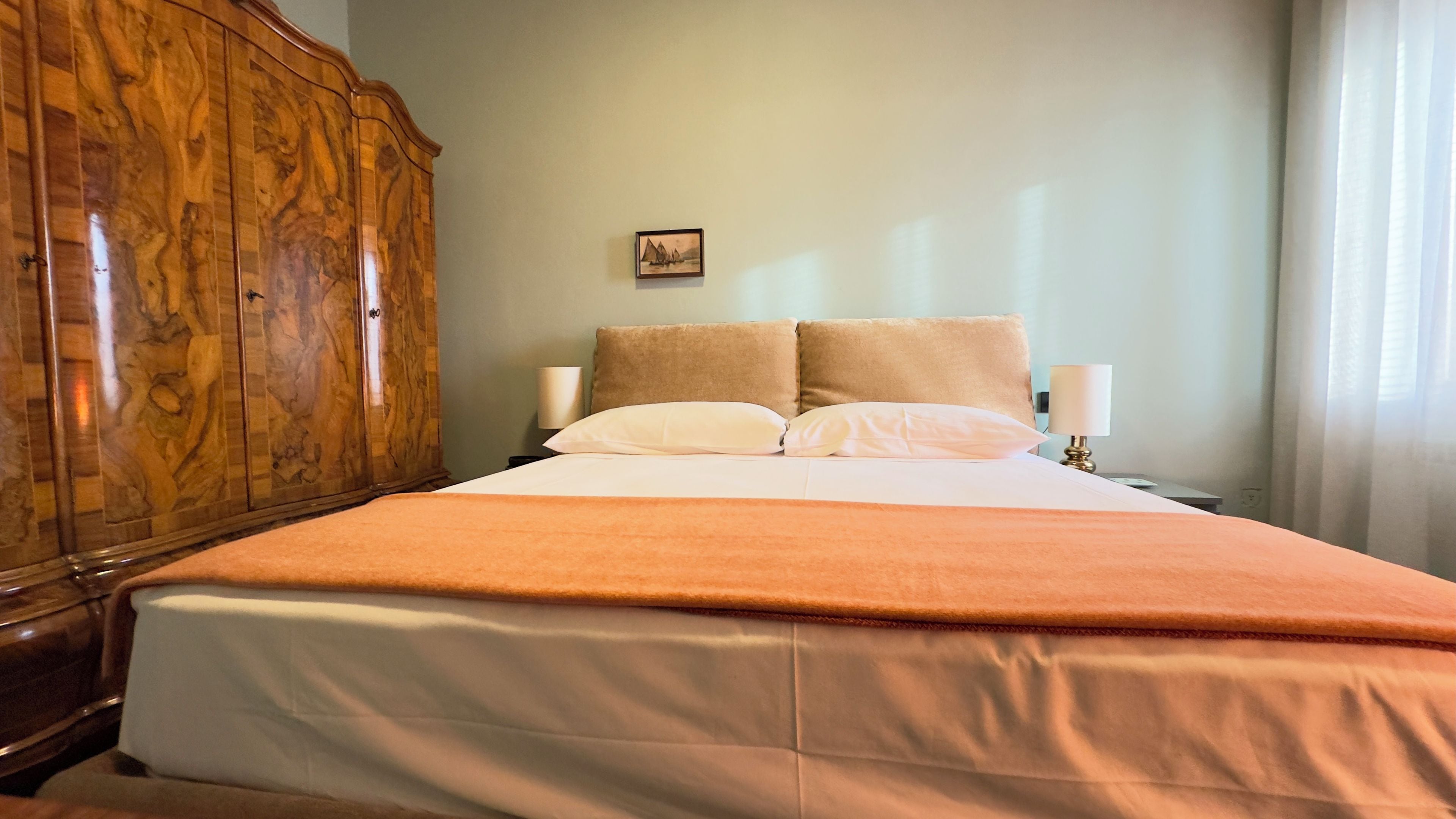 Une chambre d’hôtel avec une grande armoire en bois, un lit avec une literie blanche, deux oreillers et un petit tableau encadré accroché au mur.