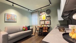 A modern living room with a grey sofa, a dining table with chairs, and a kitchen area with a sink and countertop. - Novo Taccheo by Ca-sa Check (Chioggia)
