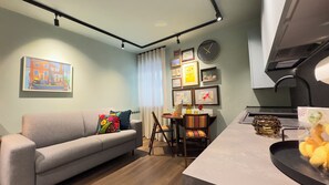 A modern living room with a grey sofa, a dining table with chairs, and a kitchen area with a sink and countertop. - Novo Taccheo by Ca-sa Check (Chioggia)