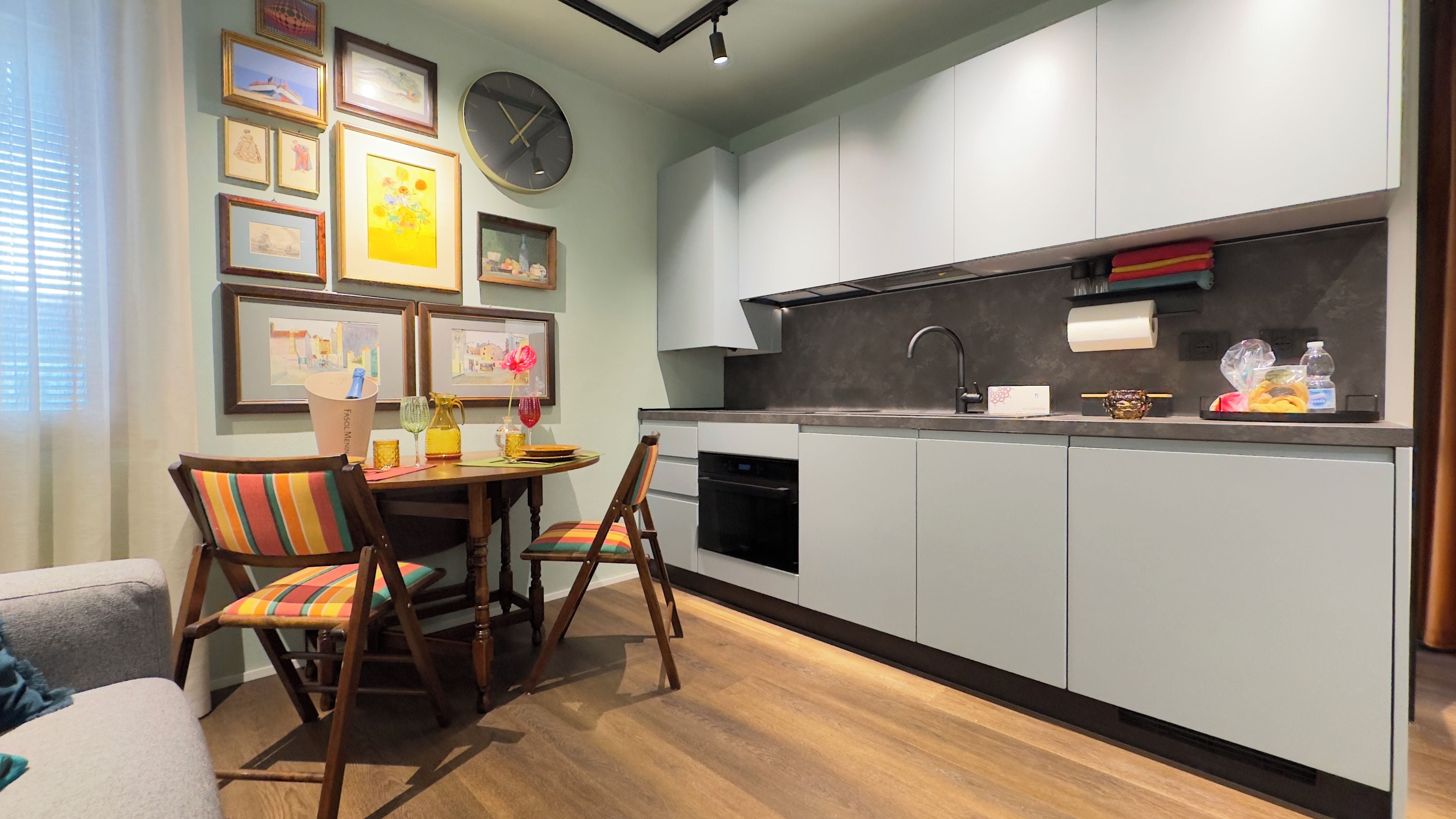 A compact kitchen with modern appliances, a dining area with a table and chairs, and a wall adorned with framed artwork.