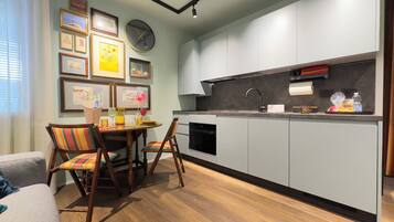 A compact kitchen with modern appliances, a dining area with a table and chairs, and a wall adorned with framed artwork.
