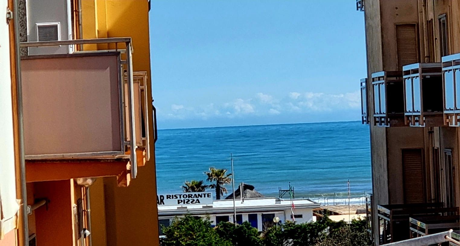 A view of the sea from a balcony with a restaurant named "Ristorante Pizza" in the background.