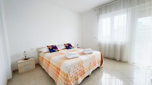 Una habitación de hotel con cama, mesita de noche, lámpara y ventana con cortinas.