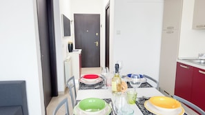 Uma área de refeições com uma mesa posta para quatro pessoas, incluindo pratos, copos e uma garrafa.