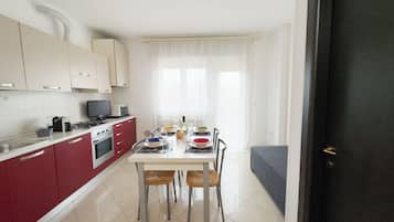 A compact kitchen with a dining area, a sofa, and a door leading to another room.