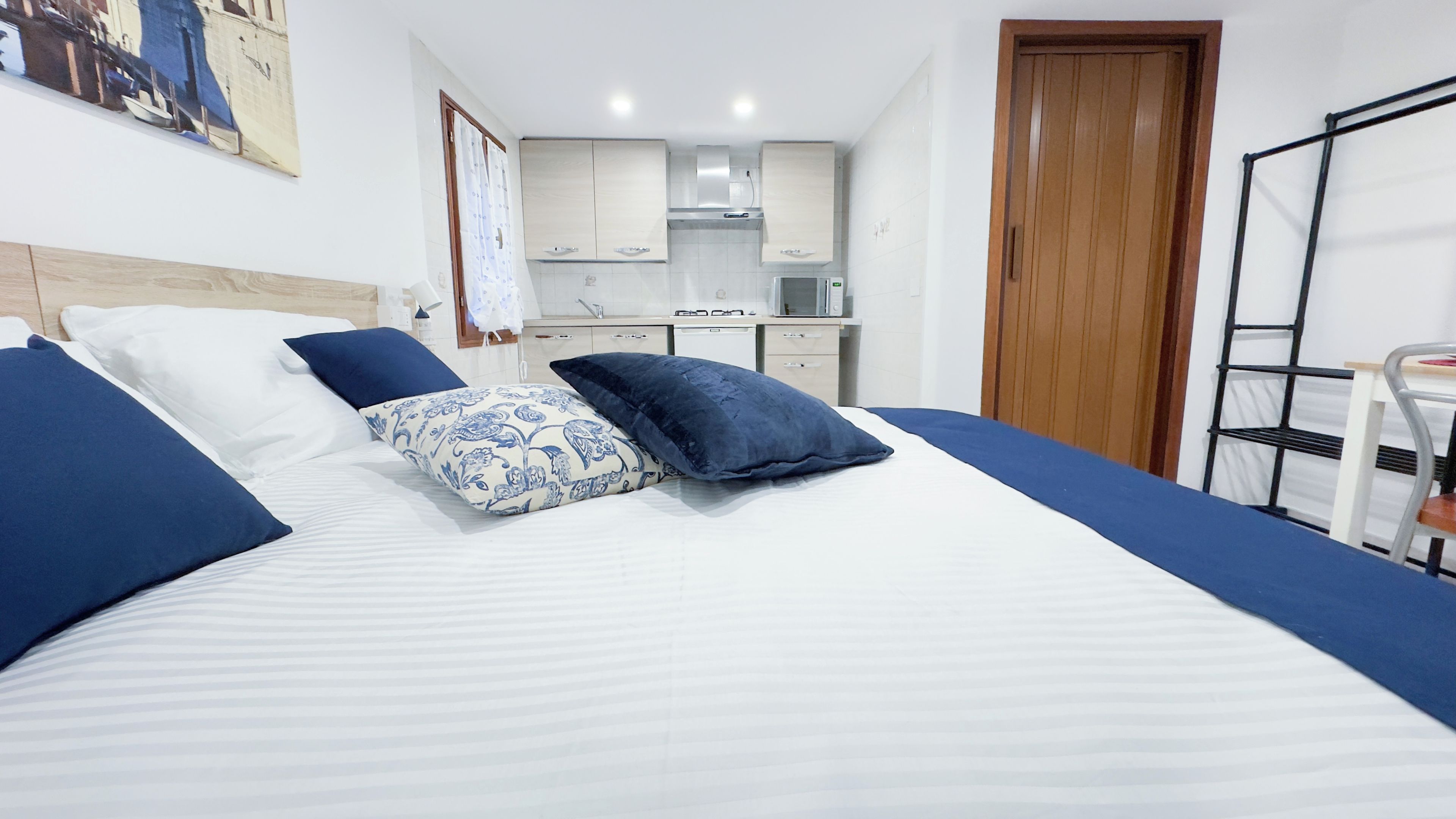 A hotel room with a bed, a wooden door, a kitchenette, and a small table.