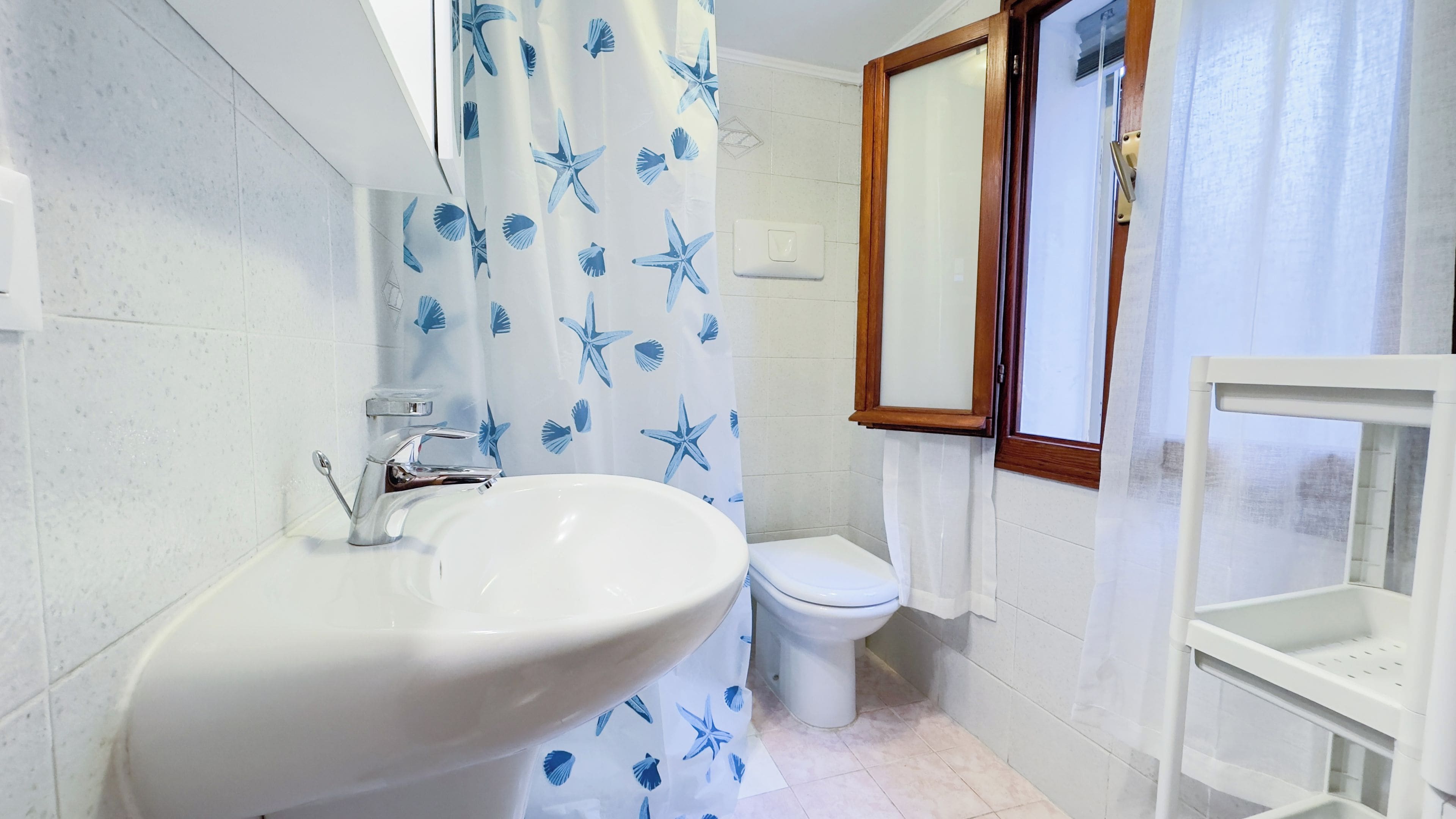 A bathroom with a white sink, a toilet, and a shower curtain with a starfish pattern.
