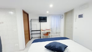 Een hotelkamer met een bed, een bureau met stoel, een aan de muur bevestigde televisie en een raam met gordijnen.