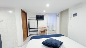Une chambre d’hôtel comprenant un lit, un bureau avec une chaise, un téléviseur fixé au mur et une fenêtre avec des rideaux.