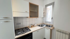 Eine kompakte Küche mit Gasherd, einer doppelten Spüle und einem Fenster mit Jalousien.