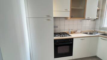 Cozinha com armários brancos, fogão a gás, forno preto e pia.