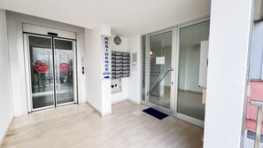 Ein Hotel Eingang mit Glastür, einer Hinweisschild für 24-Stunden-Service, einer Rezeption und einer Treppe zu einer oberen Etage.