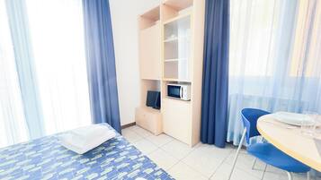 Quarto de hotel com cama, escrivaninha, micro-ondas e cadeira.