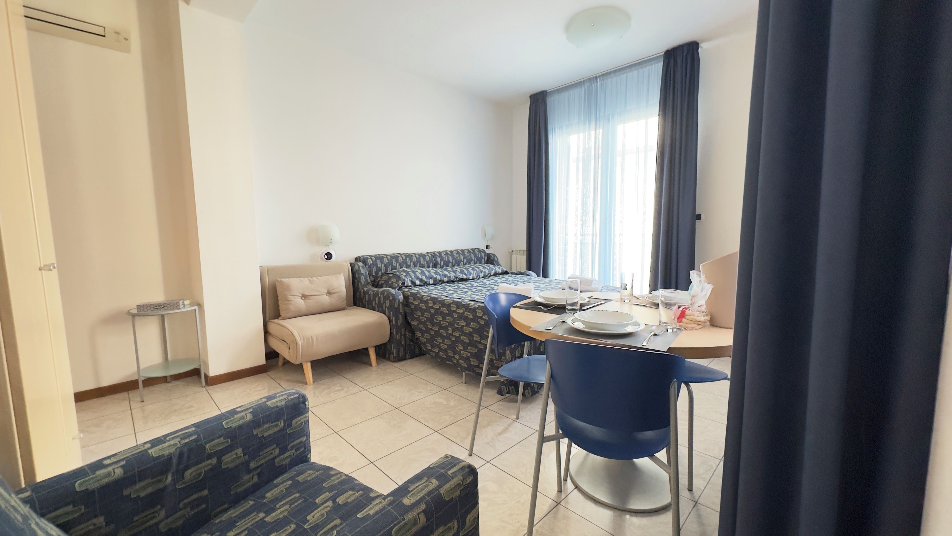 A hotel room with a bed, a desk with a chair, a small table, and a sofa.