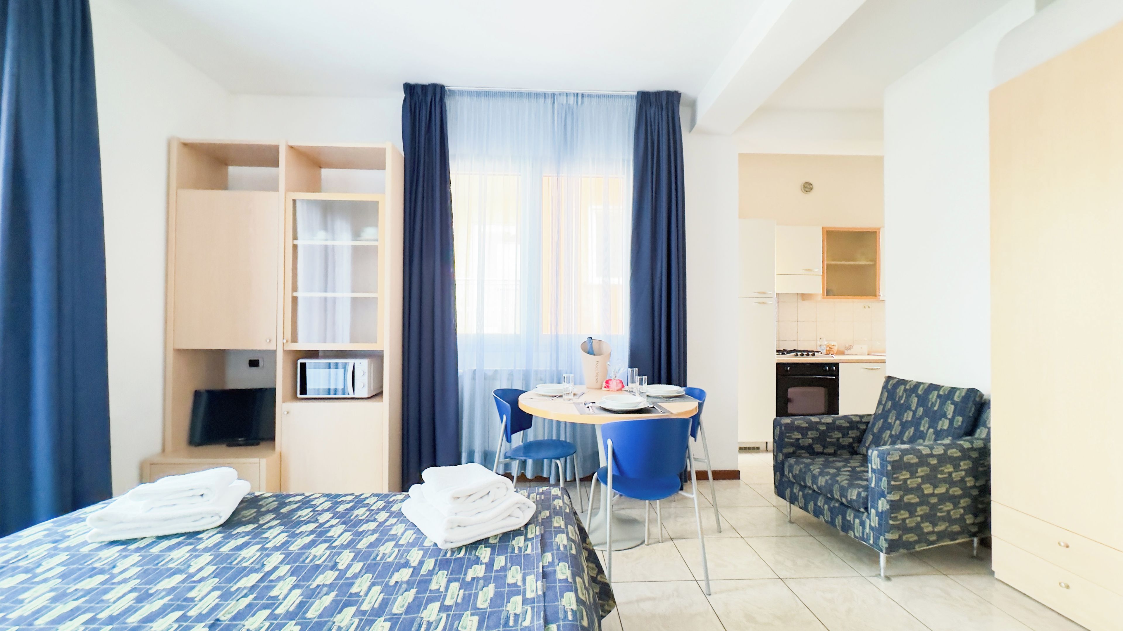 A hotel room with a bed, a desk with a chair, a kitchenette, and a bathroom.