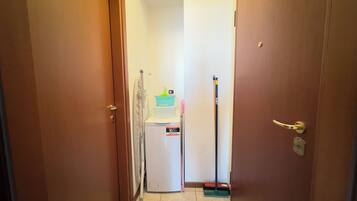 Een smalle gang met een koelkast, een dweil en schoonmaakmiddelen.