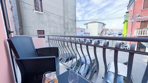 A balcony with a metal railing, two wicker chairs, a glass table, and a glass with a drink. - Alicetta Apartment by Ca-sa Check (Chioggia)