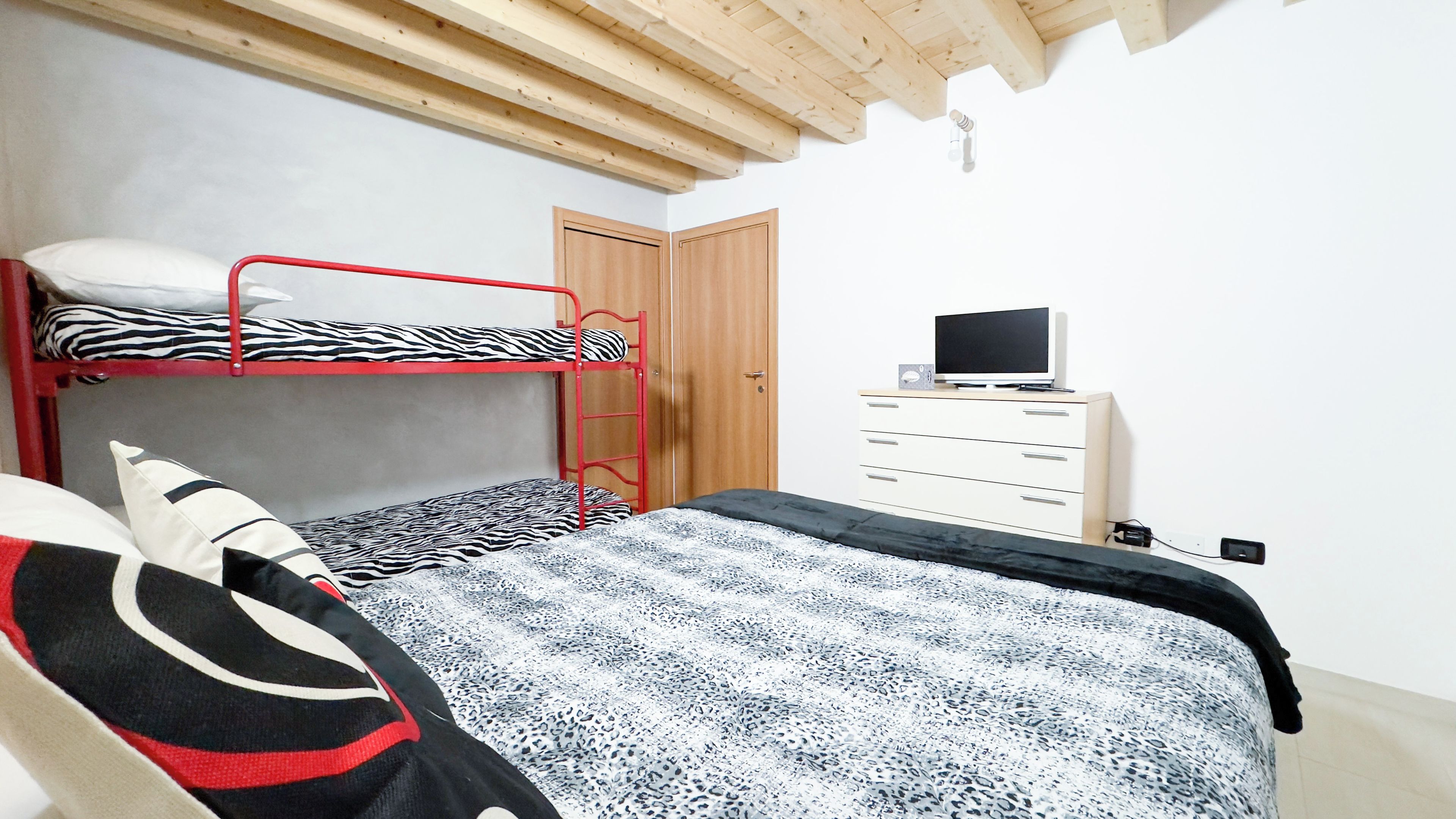 A bedroom with a bunk bed, a single bed, a dresser, and a television.