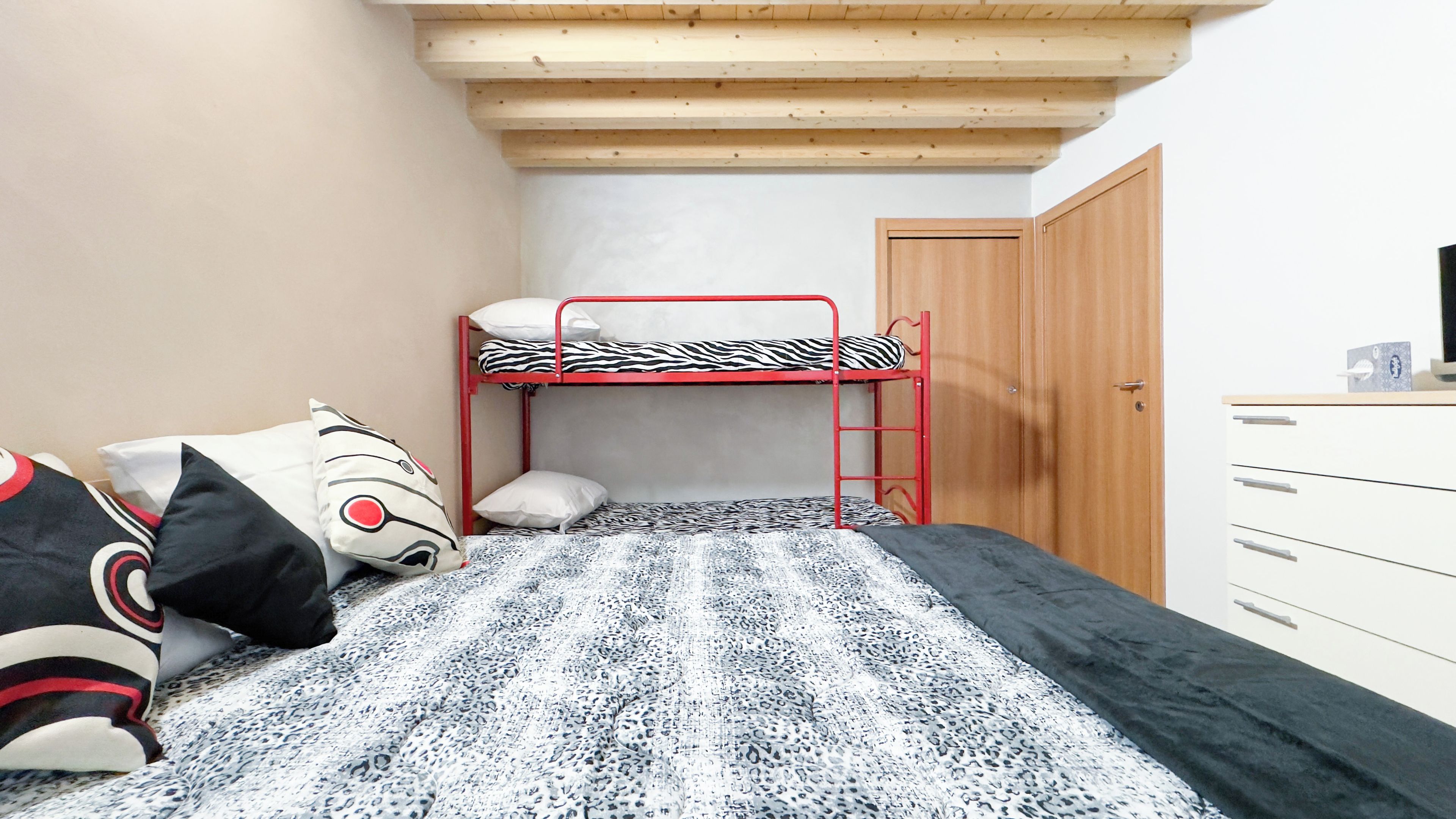 Uma cama beliche com colchão estampado em padrão de zebra, um aparador branco com gavetas e uma porta de madeira.