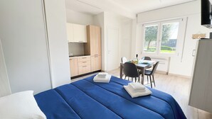A bedroom with a bed, a dining area with a table and chairs, and a kitchen in the background. - Onda Blu House by Ca-sa Check (Chioggia)